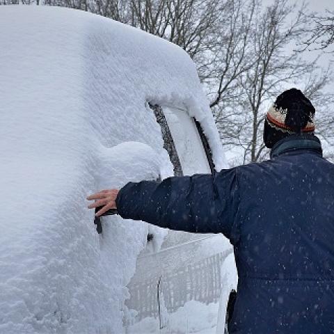 Besneeuwde auto met man die het eraf haalt